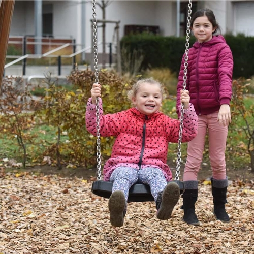 Älteres Mädchen stößt jüngeres Mädchen auf einer Schaukel auf einem Spielplatz an.