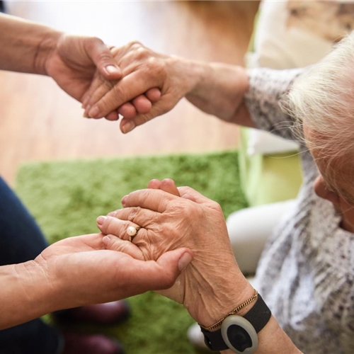 Ältere Person stützt sich zum Aufstehen auf die Hände einer helfenden Person.