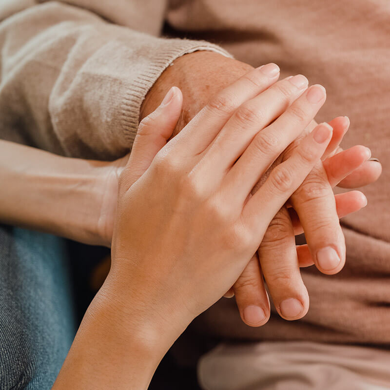 Die Hände einer jüngeren Person halten die Hand einer alten Person fürsorglich umschlossen.