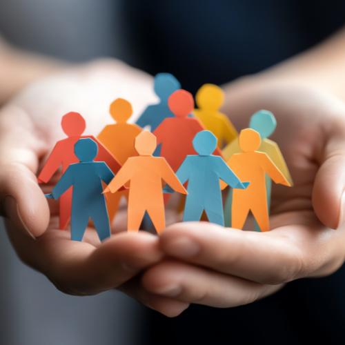 Hände, die bunte Menschen aus Papier halten und so Einheit, Teamwork und Gemeinschaft in einem vielfältigen und integrativen Umfeld symbolisieren.